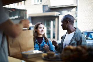 Multi-ethnic friends talking while salesman packing food at concession stand